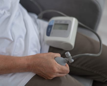 Mature Caucasian woman measuring blood pressure while sitting on sofa at home