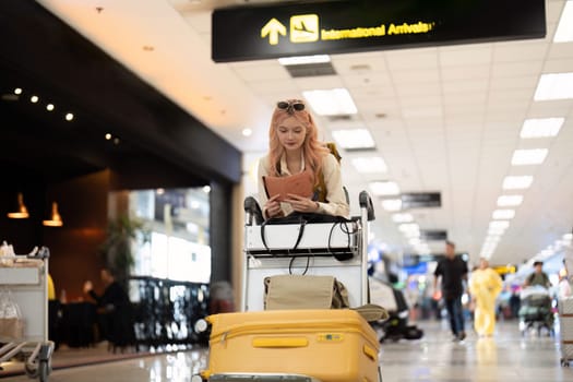 Young woman checking passport at international arrivals in airport. Casual travel, waiting for journey.