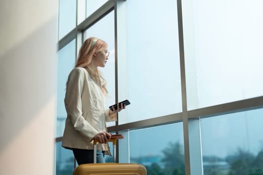 Woman traveler with luggage and phone at the airport window. Concept of travel, waiting, and departure.