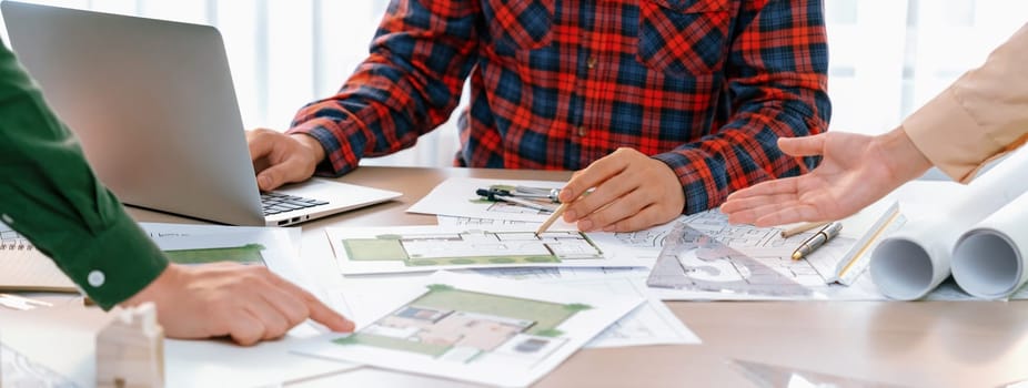 Professional architect design a blueprint by using laptop during project manager shows mistake point on table with architectural document and wooden block scatter around.. Closeup. Delineation.