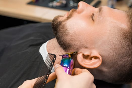 Stylist shaves gently young man neck using trimmer in barbershop closeup. Skilled barber with cutting tool serves male client in salon