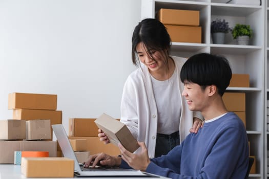 A happy Asian online shopping entrepreneur couple takes orders and packs products to send to customers together in their office..