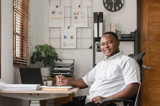 African American businessman working on paperwork, searching for information with laptop at home office.