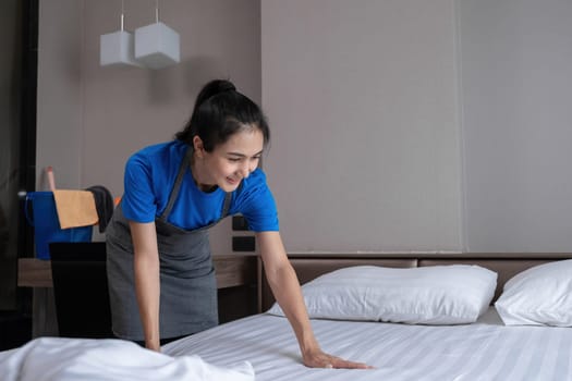 The hotel housekeeper in the room was cleaning the bed and preparing the bedding..