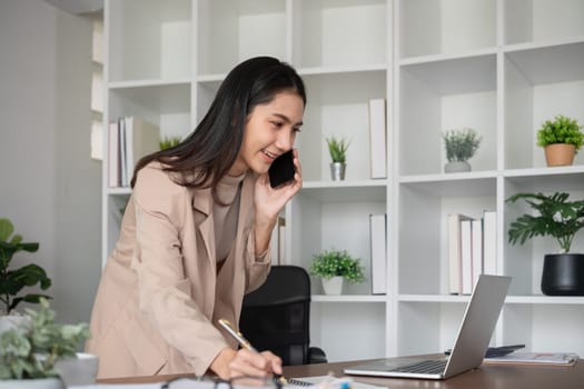 Asian businesswoman talking on the phone, having an online business meeting in a modern home office..