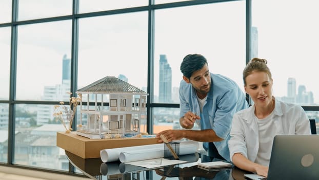 Smart architect engineer inspect house model while colleague using laptop analysis data. Professional designer team working together to design house model construction at modern office. Tracery