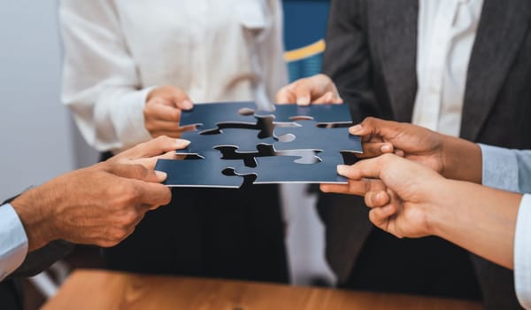 Corporate officer worker collaborate in office, connecting puzzle pieces with report paper on table as partnership and teamwork. Unity and synergy in business concept by merging jigsaw puzzle. Concord