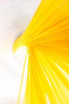 A bunch of bright yellow spaghetti arranged in a glass on a clean white surface, top view