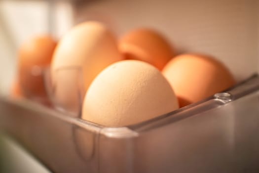 Organic eggs are stored in a transparent container inside a fridge, used as a key ingredient in various dishes, an oval staple food in different cuisines