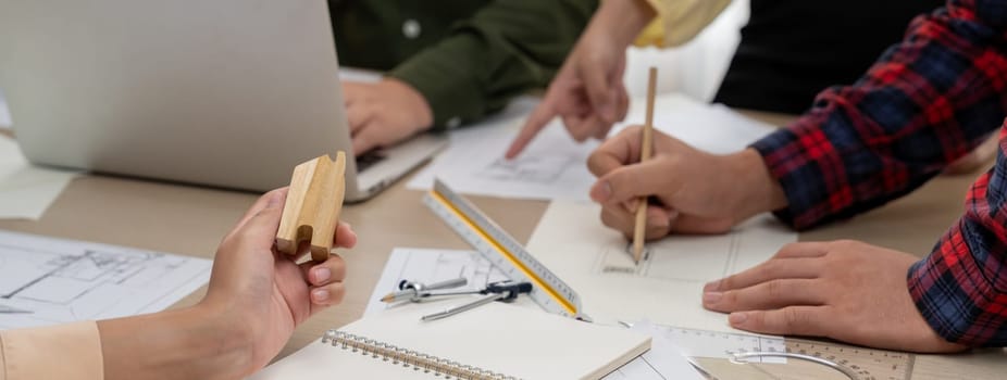 Professional architect team discussion about architectural project on meeting table with blueprint and wooden block scatter around at modern office. Closeup. Focus on hand. Delineation.