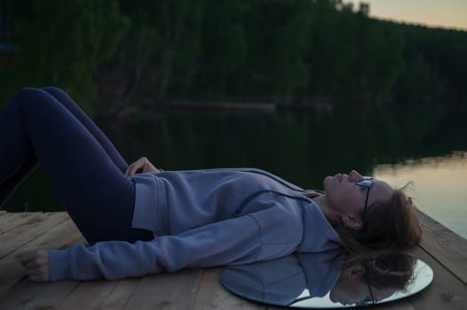 Woman lying down on the pier at lake, closeup portrait, summer sunset