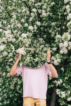 Creative male portrait with mirror in a blooming apples spring garden