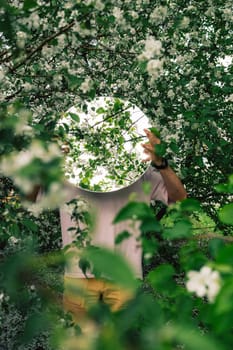 Creative male portrait with mirror in a blooming apples spring garden