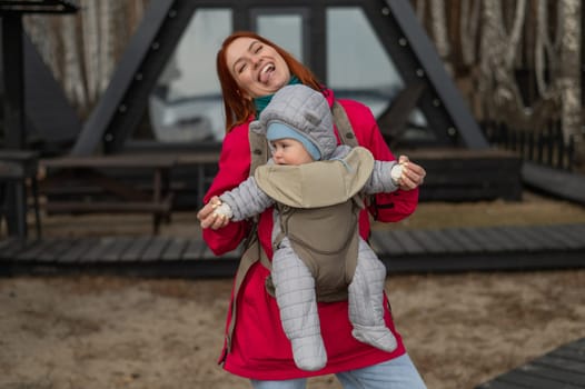 A Caucasian woman walks with her son in an ergo backpack in the countryside