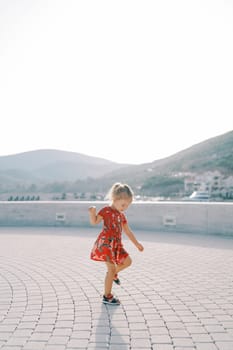 Little girl walks along a paved embankment looking at her feet. High quality photo