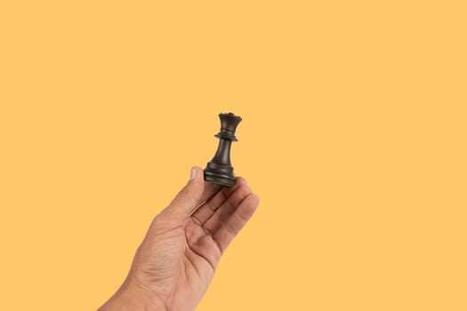 Black male hand holding a black queen chess figure isolated on yellow background. High quality photo