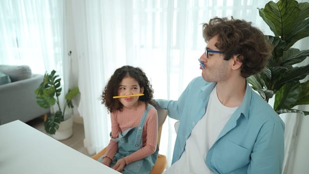 Funny caucasian dad and american kid doing funny face while put pencil between lip and nose. Cute family study about writing engineering prompt together and generating AI at laptop on table. Pedagogy.