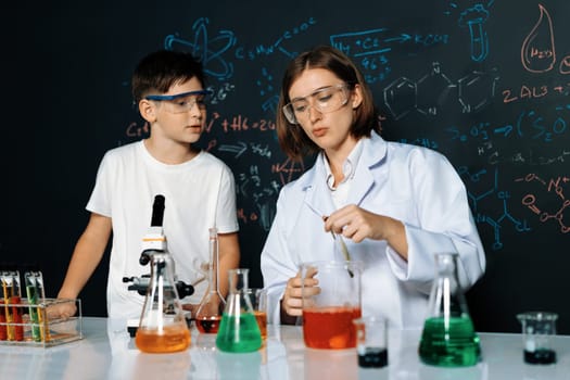 Teacher support schoolboy in laboratory. Schoolboy and teacher stand and experiment about science of chemistry in STEM class using liquid in glass container. Instructor mixing solution. Erudition.