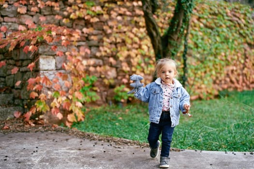 Little girl walks along a paved path in the park with a toy in her hand. High quality photo