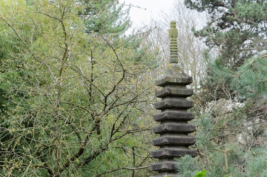 Tall, slender stone tower with a pointed roof stands amidst a dense green forest. Moss and climbing vines cover the towers exterior, creating a sense of age and mystery.