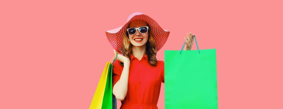 Portrait of beautiful happy smiling young woman model posing with colorful shopping bags wearing summer straw hat, dress on pink studio background