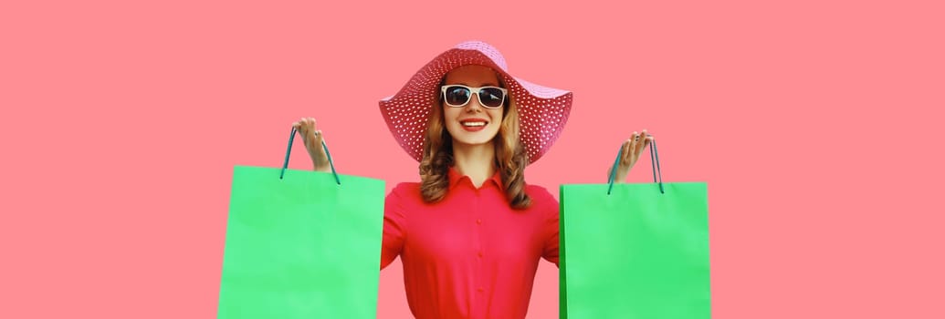 Portrait of beautiful happy smiling young woman model posing with colorful shopping bags wearing summer straw hat, dress on pink studio background