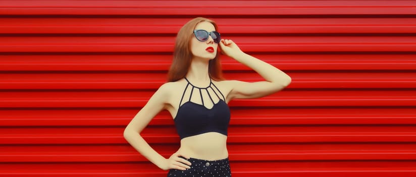 Portrait of stylish caucasian young woman model posing in black outfit, sunglasses on red background