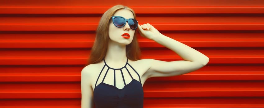 Portrait of stylish caucasian young woman model posing in black outfit, sunglasses on red background