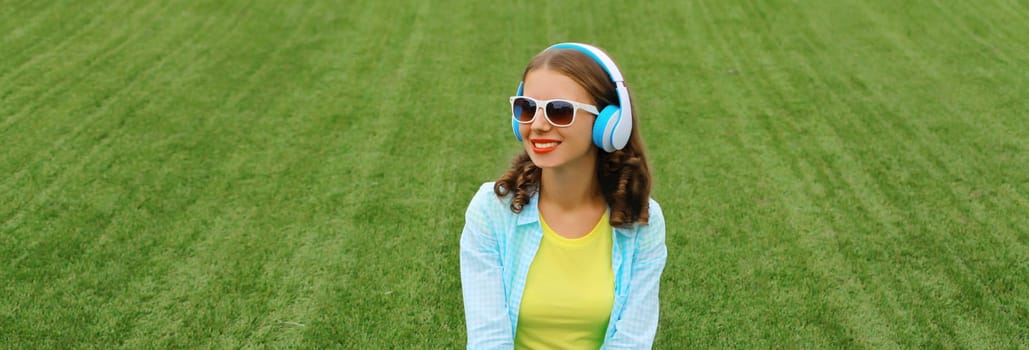 Portrait of happy smiling young woman listening to music in headphones while lying on grass in summer park