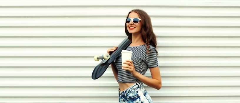 Portrait of stylish young woman with skateboard and cup of coffee on white background