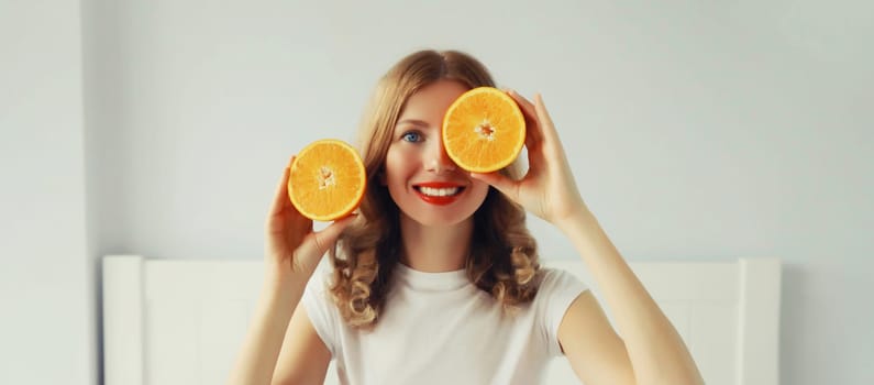 Summer, nutrition, diet and vegetarian concept. Happy healthy cheerful young woman with slices of orange fruits in white room at home