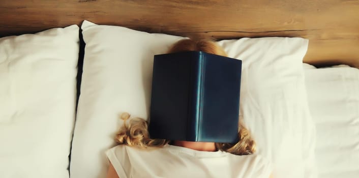 Young sad tired woman student covering her face with open book with blank cover while lying on the bed at home