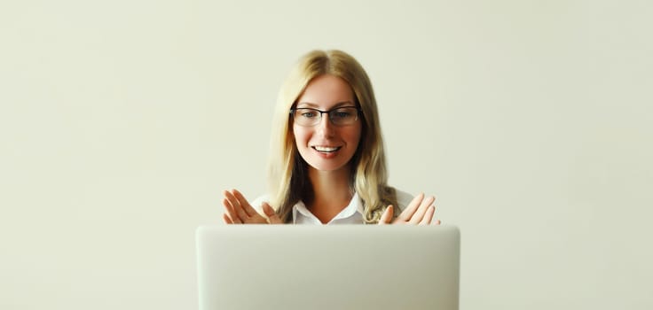 Happy young woman working on laptop greets communicates with friends via video call sitting at desk in office or home