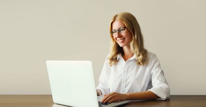 Happy young woman working with laptop sitting at desk in office or home