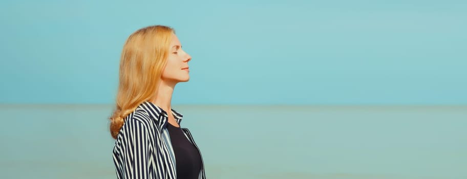 Calm relaxing healthy young woman meditates, practicing breathing exercises enjoying fresh air on the beach on sea coast and blue sky background