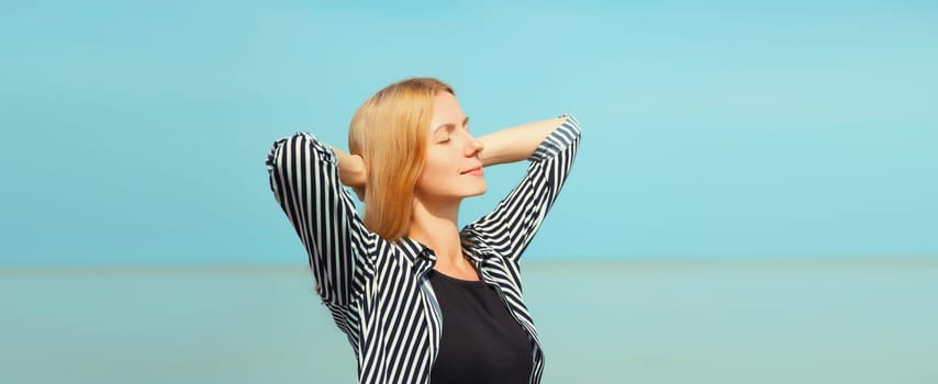 Summer vacation, happy relaxing healthy young woman meditates and enjoying fresh air on the beach on sea coast and blue sky background