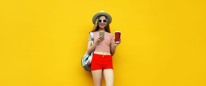 Summer image of traveler young woman 20s full length with mobile phone looking at device in casual straw hat with backpack on bright yellow background