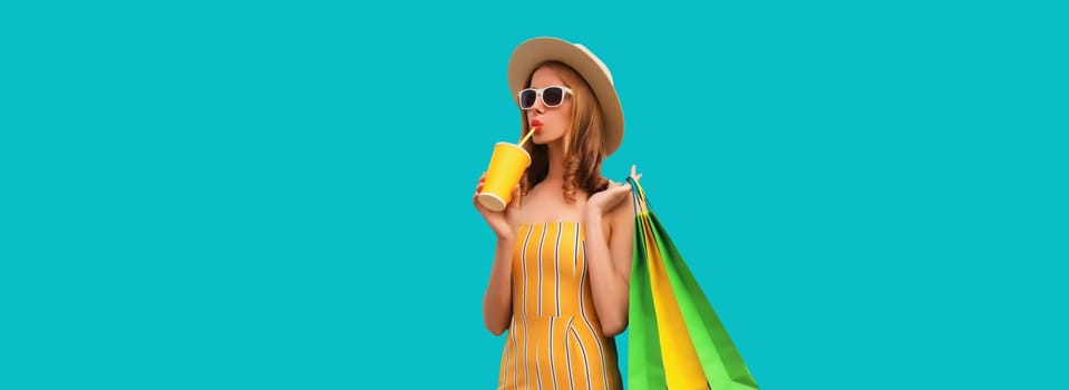 Portrait of beautiful relaxed young woman model with colorful shopping bags drinking juice in summer straw hat on blue studio background