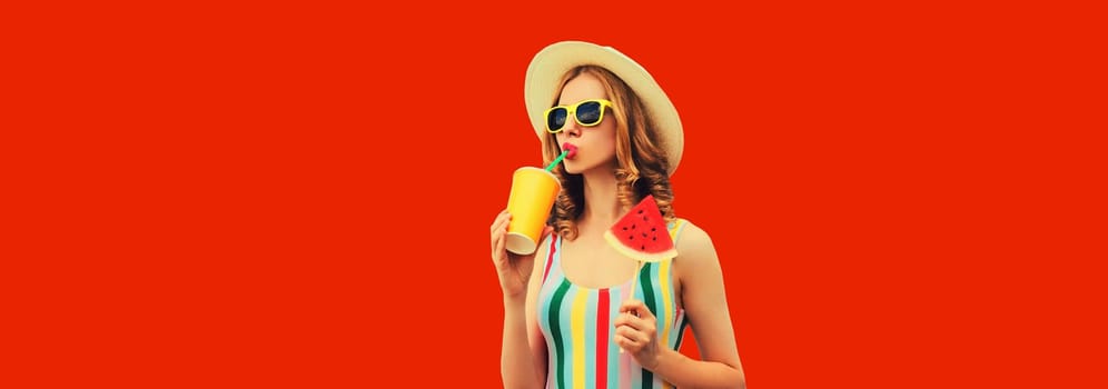 Summer portrait of young woman drinking juice with sweet juicy lollipop or ice cream shaped slice of watermelon wearing straw hat on red background, blank copy space