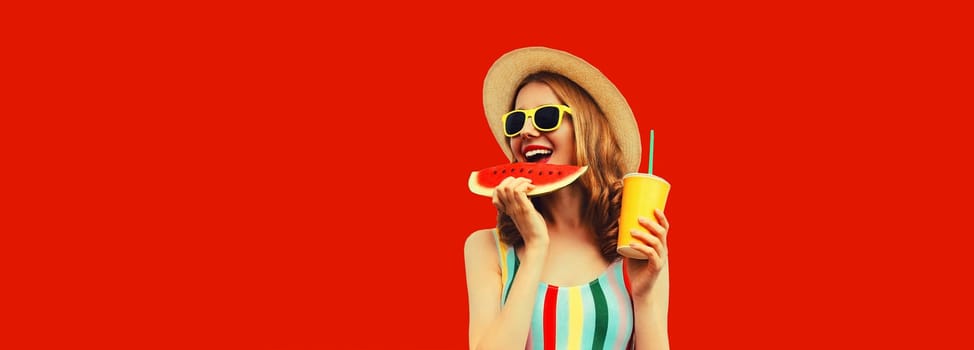 Summer portrait of happy smiling young woman eating fresh juicy slice of watermelon with cup of juice wearing tourist straw hat on red background