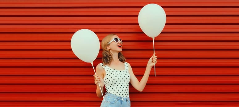 Summer, holiday, celebration, happy cheerful young woman with bright colorful balloons wearing white heart shaped sunglasses having fun on red background