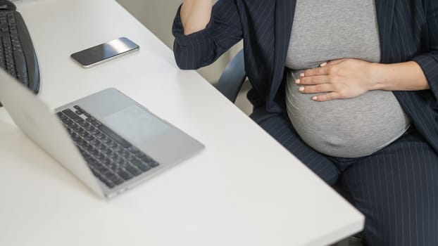 A pregnant woman works on a laptop in the office. Close-up of the tummy