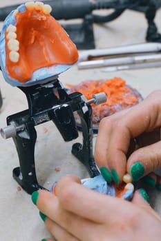 The hands of an orthodontic dental technician make a denture by working with molten liquid wax. Close-up