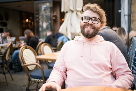 Millennial bearded man having breakfast at table of street cafe on spring day, drinking warm cappuccino. Spring restaurant terrace.