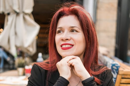 Beautiful happy woman with long red hair enjoying pasta in a street cafe