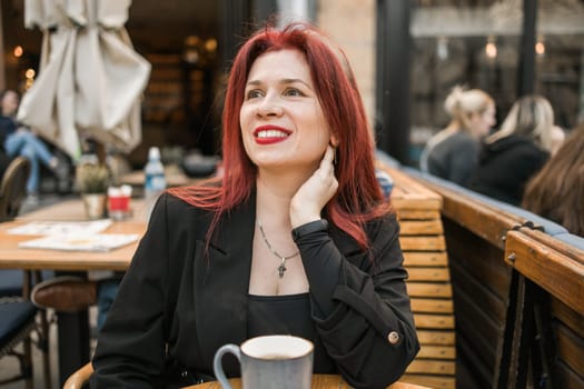 Beautiful happy woman with long red hair enjoying cocktail in a street cafe.