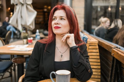 Beautiful happy woman with long red hair enjoying cocktail in a street cafe.