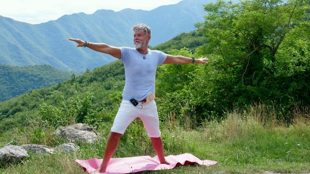 A sick old gray-haired man with diabetes and colon cancer with a colostomy practices yoga in the mountains. Stands in the pose of a warrior