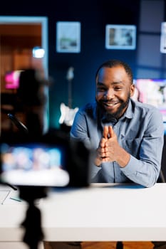 African american man filming himself with professional camera, watching internet videos requested by followers. Media star laughing while reacting to online clips sent by subscribers