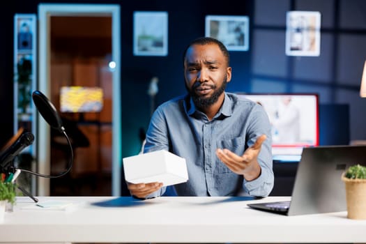 BIPOC tech content creator filming technology review of newly launched smartphone, unboxing it and presenting specifications to audience. Influencer showing mobile phone to viewers